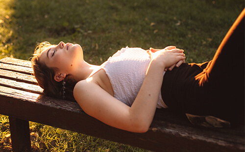 Eine Frau liegt auf einer Bank in der Sonne