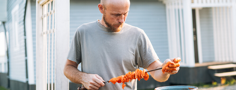 Ein Mann bestückt einen Spieß zum Grillen mit Fleisch. 