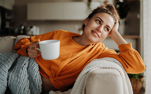 Eine Frau mit einer Tasse in der Hand auf der Couch. 