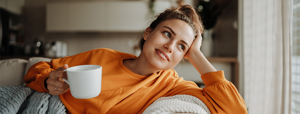 Eine Frau liegt mit einer Tasse in der Hand auf der Couch. 