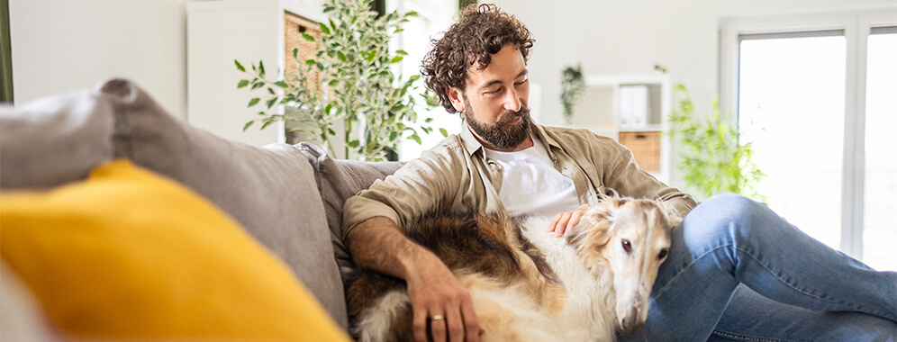 Ein Mann kuschelt mit seinem Hund auf der Couch. 
