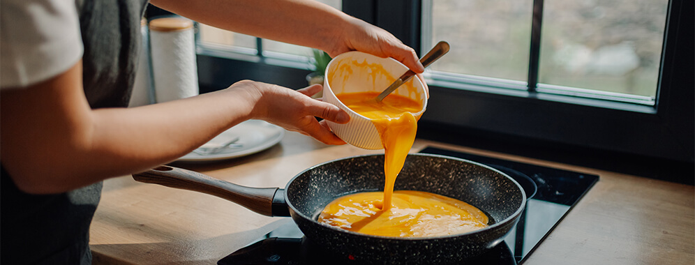 Jemand schüttet eine gelbe Flüssigkeit in eine Pfanne.