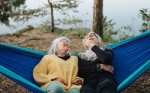 Zwei Frauen liegen in einer Hängematte und lachen. 
