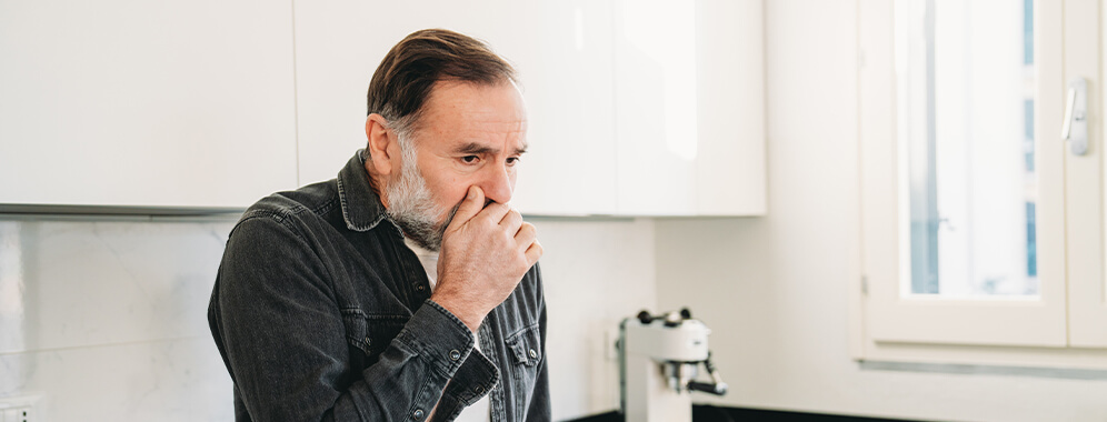 Ein Mann steht hustend in der Küche.