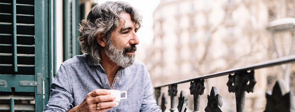 Ein Mann trinkt einen Kaffee auf einem Balkon sitzend.
