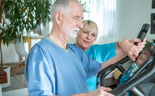 Eine Frau erklärt einem älteren Herrn die Einstellungen auf einem Cardio-Sportgerät.