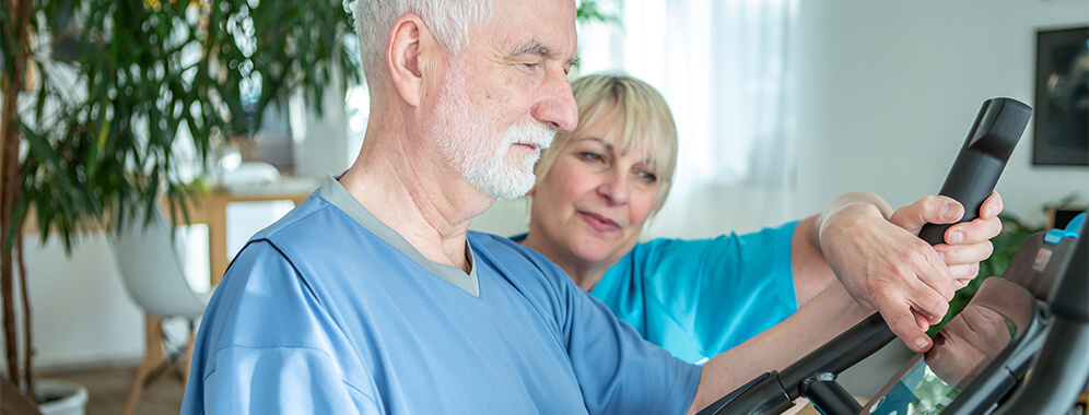 Eine Frau erklärt einem Mann die Einstellungen eines Cardio-Sportgeräts