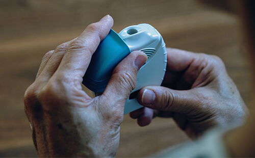 Eine Person hält einen Inhalator in der Hand. 