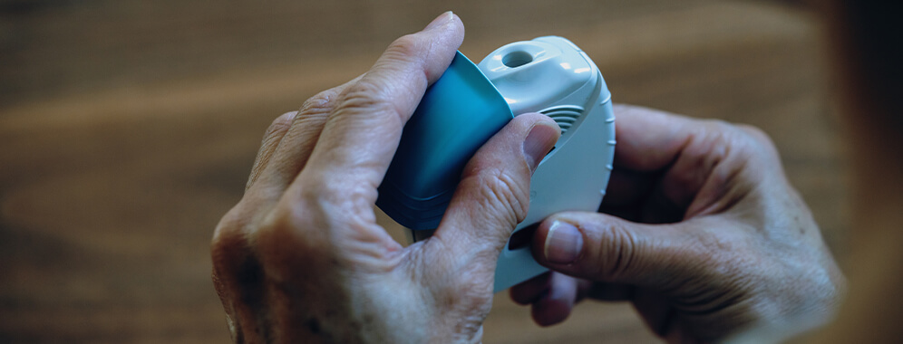 Eine Person hält einen Inhalator in der Hand. 