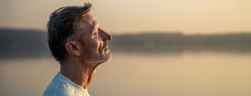 Ein Mann atmet ruhig und blickt in den Sonnenuntergang