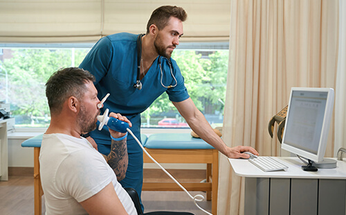 Ein Mann atmet beim Arzt in ein Gerät hinein. 