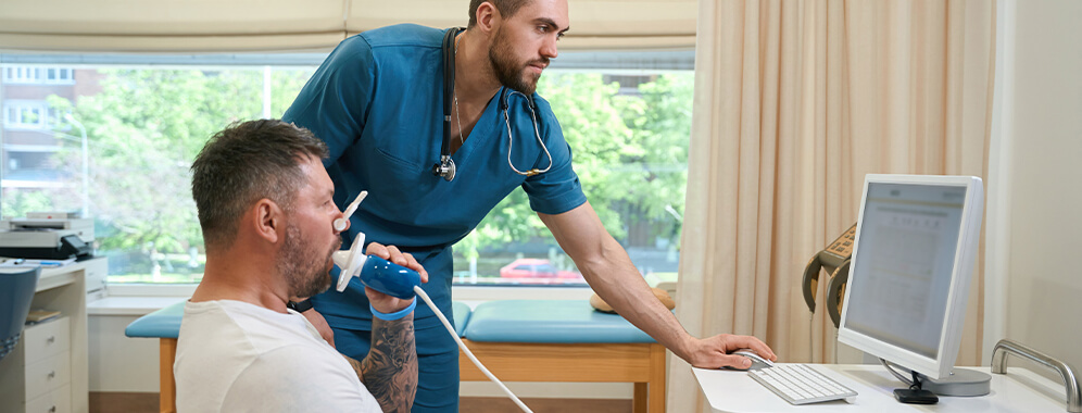 Ein Mann atmet beim Arzt in ein Gerät hinein. 