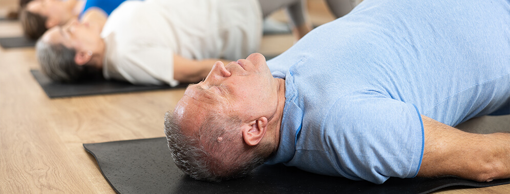 Ein Mann liegt auf einer Yogamatte und macht eine Übung.