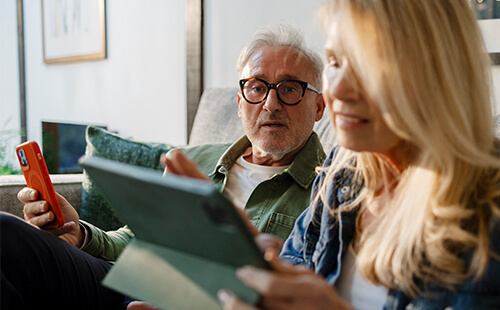 Ein Paar recherchiert etwas an Handy und Tablet.