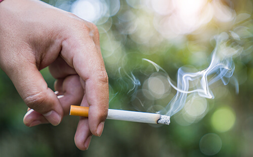 Eine Hand hält eine brennende Zigarette.