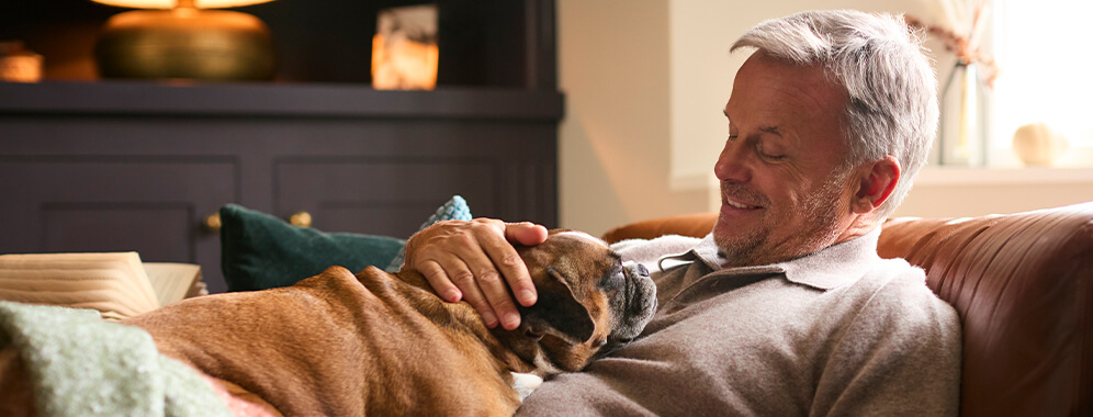 Ein Mann kuschelt mit seinem Hund auf der Couch. 
