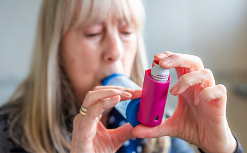 Eine Frau inhaliert mithilfe eines Spacers.