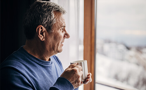 Ein Mann hält eine Tasse und blickt aus dem Fenster.