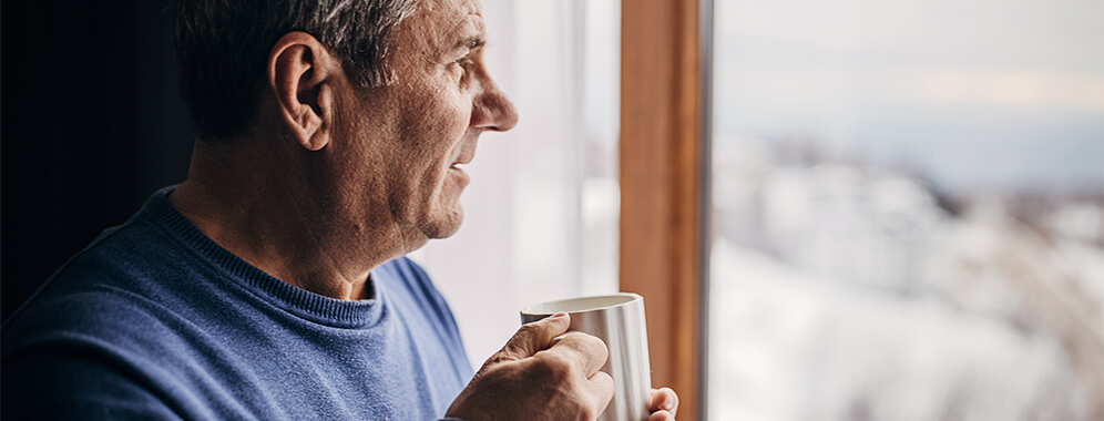 Ein Mann hält eine Tasse in der Hand und blickt aus dem Fenster.