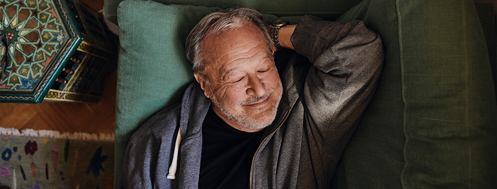 Ein Mann liegt mit geschlossenen Augen auf der Couch. 