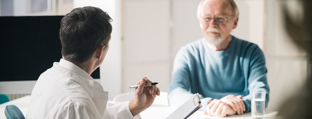 Ein älterer Mann im Gespräch mit einem Arzt in der Praxis. 