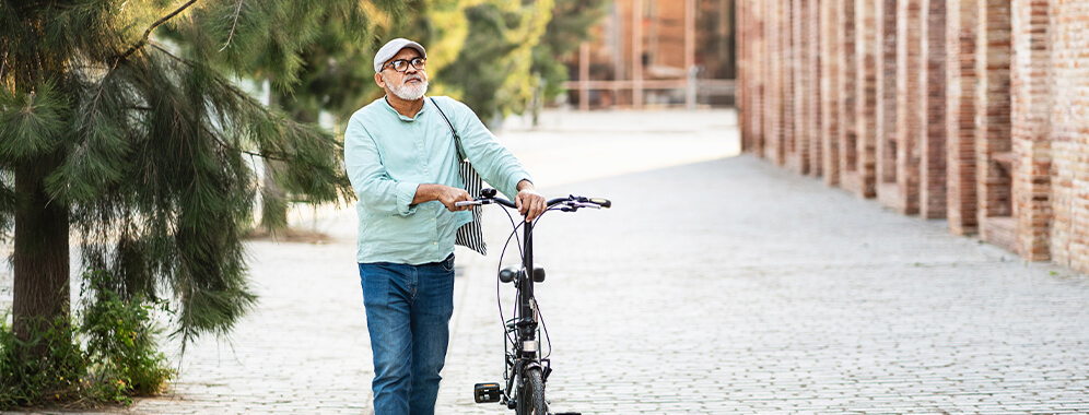 Ein älterer Mann geht durch eine Stadt und schiebt dabei ein Fahrrad.
