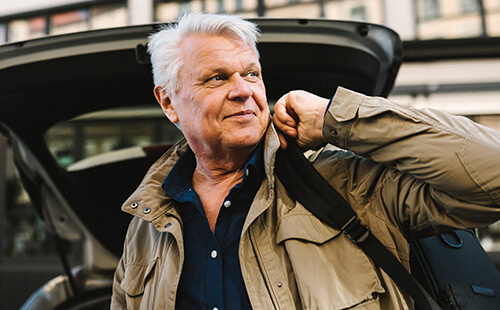 Ein älterer Herr trägt Taschen aus einem Auto heraus.