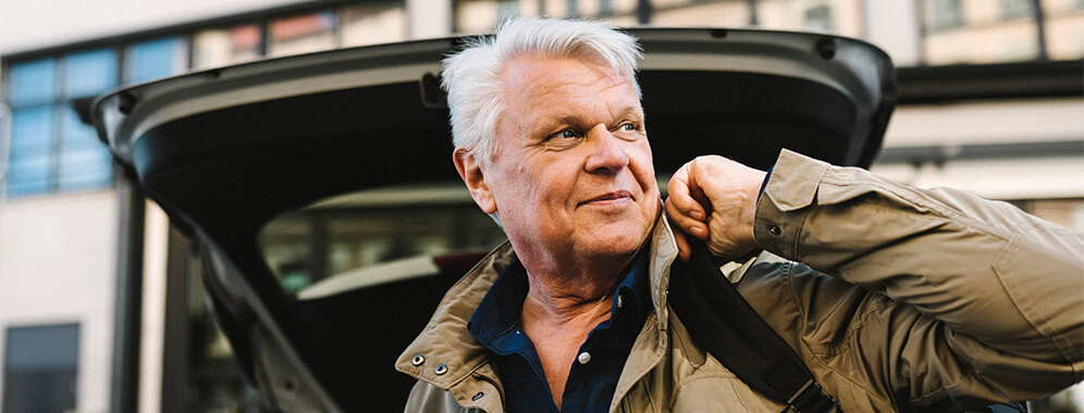 Man sieht einen Mann, der an seinem Kofferraum steht. 