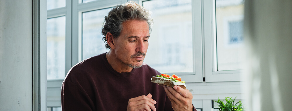 Ein Mann isst eine Scheibe Vollkornbrot mit Tomaten und Gurken belegt. 