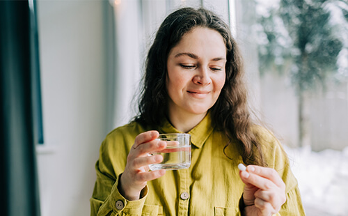 Eine Frau hält eine Abnehmpille in der einen und ein Glas Wasser in der anderen Hand.