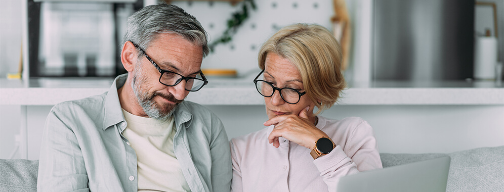 Ein Pärchen sitzt mit Formularen auf der Couch und unterhält sich darüber.