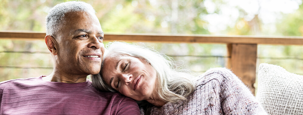 Ein Pärchen sitzt gemeinsam auf dem Sofa, die Frau lehnt sich an die Schulter des Mannes.