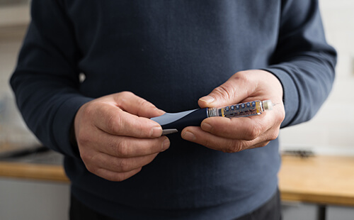 Man sieht den Oberkörper eines Mannes, der eine Insulinpen in der Hand hält. 