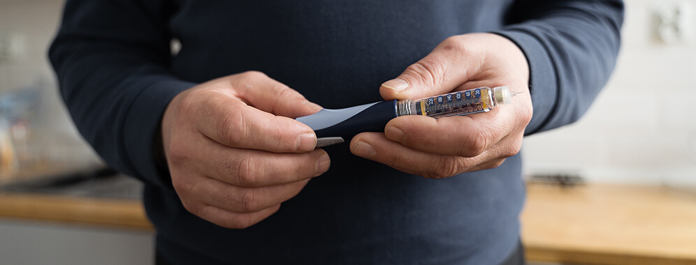 Man sieht den Oberkörper eines Mannes, der eine Insulinpen in der Hand hält.