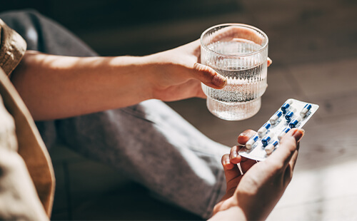 Frauenhände halten einen Tablettenblister und ein Glas Wasser.