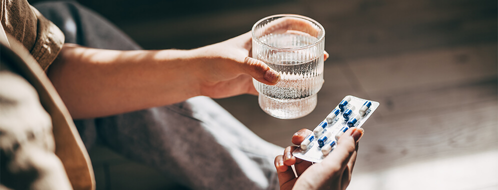 Frauenhände halten einen Tablettenblister und ein Glas Wasser.