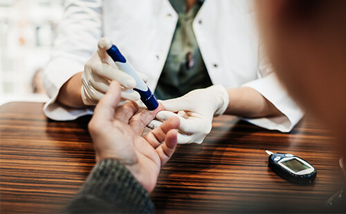 Medizinisches Personal misst mit einem Pen den Blutzuckerspiegel an der Hand eines Patienten. 