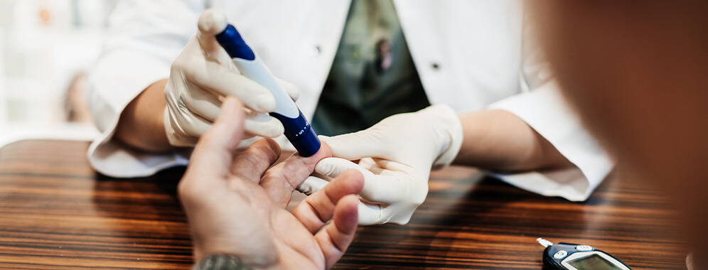 Medizinisches Personal misst mit einem Pen den Blutzuckerspiegel an der Hand eines Patienten.