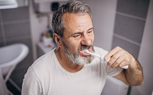 Man sieht einen Diabetiker, der sich mit einer elektrischen Zahnbürste im Badezimmer die Zähne putzt. 
