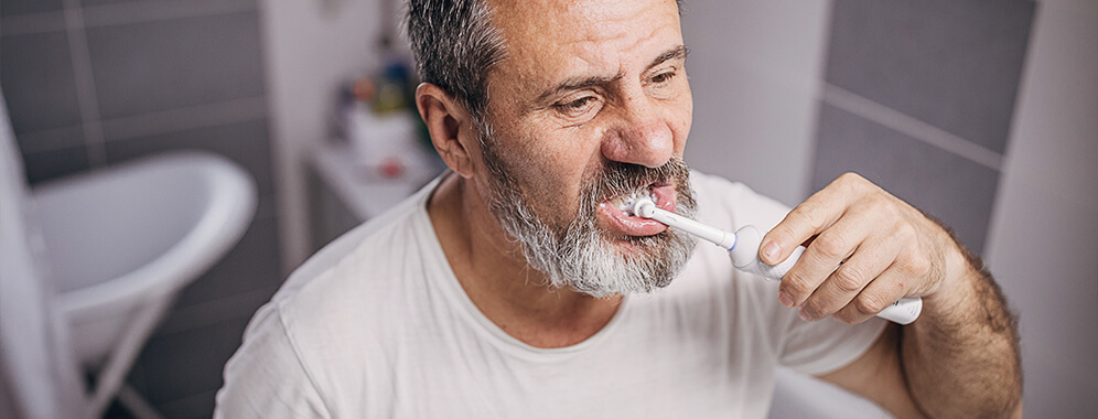 Man sieht einen Diabetiker, der sich mit einer elektrischen Zahnbürste im Badezimmer die Zähne putzt. 