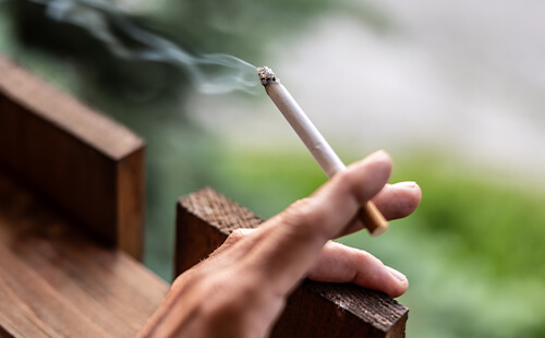 Man sieht eine Hand, die eine brennende Zigarette in der Hand hält (Nahaufnahme).