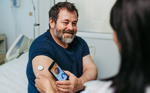 Man sieht einen Diabetiker im Gespräch mit der Ärztin, sie schauen sich die Ergebnisse der Blutzuckerwerte auf dem Handy an. 