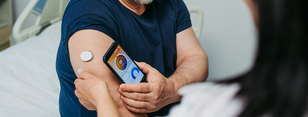 Man sieht einen Diabetiker im Gespräch mit der Ärztin, sie schauen sich die Ergebnisse der Blutzuckerwerte auf dem Handy an.