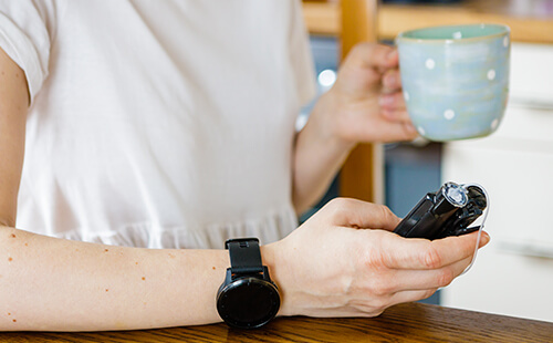 Eine Frau hält ein Device in der Hand, am Arm trägt sie eine Smartwatch.