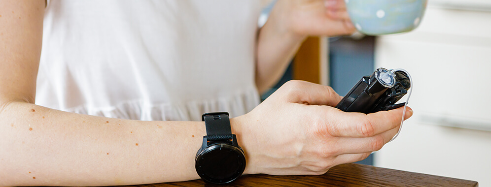 Eine Frau hält ein Device in der Hand, am Arm trägt sie eine Smartwatch.