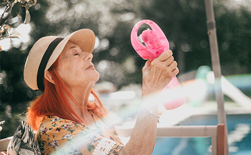 Eine ältere Dame mit Diabetes kühlt sich mit einem kleinen Ventilator ab.
