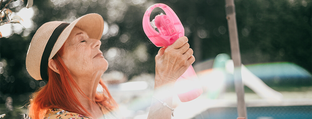 Eine ältere Dame mit Diabetes kühlt sich mit einem kleinen Ventilator ab.