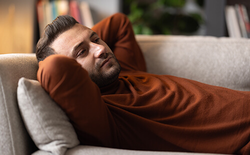 Ein Mann liegt nachdenklich auf der Couch.