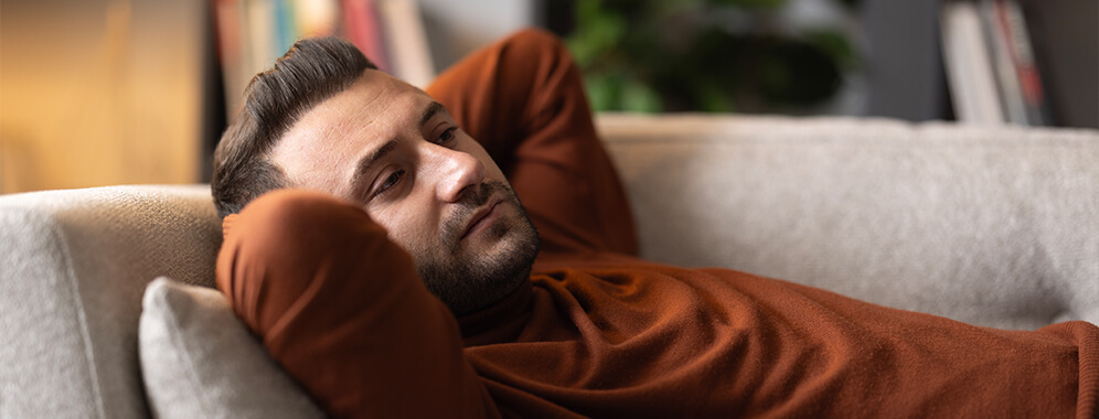 Ein Mann liegt auf der Couch und sieht nachdenklich aus.