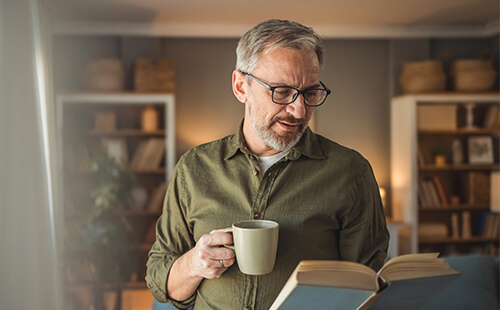 Ein Mann mit einer Tasse in der Hand liest in einem Buch.